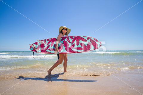 A Hispanic woman wearing swimwear while holding a surfboard on the beach attractive, beach, coast, female, girl, happy, hispanic, holiday, leisure, lifestyle, ocean, people, person, pretty, sand, sea, summer, surf, swim, vacation, voard, water, wear, woman, young
