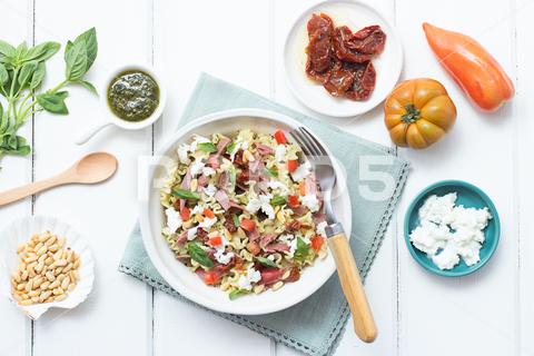 From above appetizing salad mixed with various fresh ingredients on wooden white table herb, culinary, gastronomy, spring, fusilli, lunch, recipe, cheese, bowl, leaves, basil, overhead, italian cuisine, pasta salad, dried tomatoes, mozzarella, white wood, pinions, pesto sauce, top view, summer, prosciutto, ham, tomatoes, ingredients, dinner, pasta, vegetable, salad, fresh, healthy, meal, food, cuisine, plate, background, olive, italian, cooked, mediterranean, green, table, organic, diet, oil, tasty, delicious