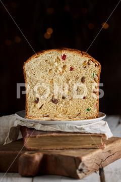 Still life of sliced fresh baked artisan Christmas panettone cake on vintage book and cutting board against dark background panettone, traditional, dessert, christmas, cake, piece, bake, bread, food, homemade, italian, recipe, bakery, kitchen, meal, cuisine, holiday, rustic, artisan, typical, fruit, pie, handmade, pastry, xmas, culinary, kulich, cooking, sweet, festive, gourmet, gastronomy, delicious, copy space, blurred, selective focus, whole, sliced, dark background, bright, plate, table, breakfast, bokeh, dim, still life, vintage
