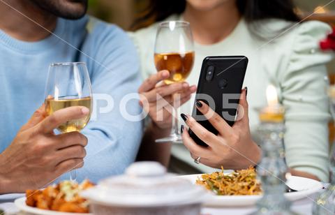 Close up shot of couple hands using mobile phone by having drinks during candlelight dinner - concept of wedding anniversary celebration, cyberspace and dating application. couple, using, wedding, anniversary, app, romance, dating, celebrate, application, drinking, mobile phone, romantic, luxury, enjoyment, dining, marriage, holidays, party, wine, india, love, girlfriend, boyfriend, celebration, valentines, friends, bonding, smiling, valentine, asian, social media, husband, internet, unrecognizable, candlelight, wife, married, indian, dinner, restaurant, wineglass, home, smartphone, online, affectionate