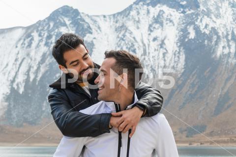 Smiling young homosexual couple looking at each other while standing and embracing near lake against mountain ridge {{couple,homosexual,relationship,embrace,smile,love,gay,hug,lake,mountain,ridge,nature,together,romantic,affection,happy,fondness,lgbt,partner,young,cheerful,romance,bonding,same sex,tender,glad,beloved,gentle,amorous,enjoy,date,cuddle,trip,stand,male,in love,pond,tourism,travel,range,looking at each other,outdoors}}