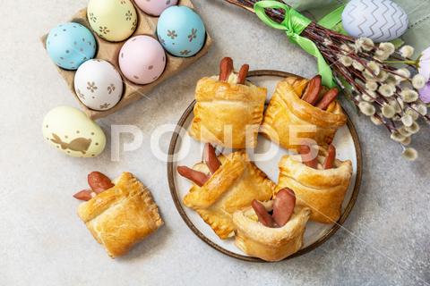 Buns in the form of an Easter rabbit from sausage and cheese in a yeast dough with colored eggs on a gray stone background. Traditional Easter symbols and food. View from above. baked, holiday, easter, food, homemade, rabbit, table, celebration, background, bread, tasty, bunny, bun, meal, snack, spring, traditional, festive, dessert, pastry, symbol, wooden, springtime, lunch, cake, sausage, happy, breakfast, dinner, seasonal, brunch, cheese, meat, sauce, eggs, colorful, concept, rustic, plate, healthy, funny, creative, easter food, easter party, easter eggs, bakery, buns, easter bunny