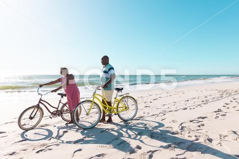 African american senior couple with bikes walking and talking at beach against clear sky in summer. Copy space, travel, unaltered, vacation, love, together, retirement, nature, active lifestyle. Two People, Senior, Elderly, Man, Male, Black, Mature Adult, Woman, Female, People, African American, Senior Couple, Bike, Walking, Talking, Beach, Clear, Sky, Summer, Copy Space, Space Travel, Retired, Unaltered, Vacation, Love, Together, Retirement, Nature, Sea, Landscape, Travel, Outdoor, Water, Ocean, Beautiful, Tourism, Blue, Coast, Holiday, Sun, View, Sand, Green, Natural, Tropical, Outdoors, Sunny, Day, African, American, Couple, Copy, Space