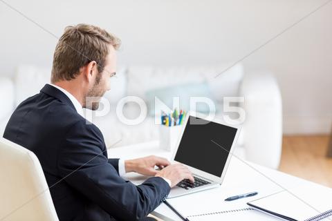 Businessman using laptop at desk in office 30s, Mid Adult, Man, Male, Caucasian, Businessman, Executive, Office, Workplace, Working, Well Dressed, Sitting, Using Laptop, Laptop, Notebook, Computer, Electronic, Touching, Browsing, Internet, Wireless Technology, Communication, Connection, Diary, Organizer, Desk, Pen, Planner, Business, Corporate, Concentration, Lifestyle, Handsome, Indoors
