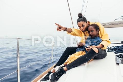 Full body of happy African American mother in casual clothes sitting on yacht and pointing away while smiling and showing view to little son during weekend mother, son, point away, yacht, smile, together, weekend, show, point, happy, boy, demonstrate, child, casual, gesture, sea, summer, parent, kid, affection, adorable, ethnic, rest, african american, childhood, cheerful, black, joy, delight, positive, bonding, relationship, motherhood, carefree, pleasure, content, love, boat, chill, full length, full body