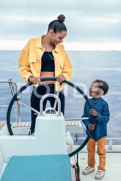 Cheerful African American mother and son standing together at steering wheel while looking at each other during weekend on yacht mother, son, yacht, steering wheel, summer, together, weekend, childhood, motherhood, cheerful, african american, smile, happy, boy, parent, ethnic, relationship, black, bonding, child, positive, joy, content, parenthood, kid, freedom, enjoy, pleasure, rest, sea, carefree, cute, sailboat, boat, vessel, vacation, spend time, chill, transport, harmony, adorable, travel, fondness, voyage, looking at each other