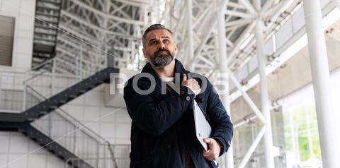 Horizontal photo of mature adult male boss with gray hair and beard walking on work site. business, man, businessman, suit, boss, office, senior, online, outside, message, serious, mature, city, building, focused, smartphone, using, reading, walking, standing, executive, manager, employee, modern, entrepreneur, professional, confident, leader, career, urban, outdoors, mature adult, beard, gray hair