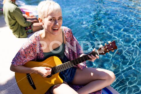 Portrait of happy caucasian woman having pool party, playing guitar and smiling in garden. Lifestyle, party and summer. Three People, Young Adult, Man, Male, Multiracial, Woman, Female, Non-Binary, White, People, Portrait, Happy, Caucasian Woman, Pool Party, Playing Guitar, Smiling, Garden, Lifestyle, Summer, Young, Person, Beautiful, Adult, Cheerful, Attractive, Nature, Happiness, Fun, Smile, Cute, Beauty, Outdoor, Pretty, Face, Leisure, Spring, Green, Healthy, Caucasian, Pool, Party, Playing, Guitar