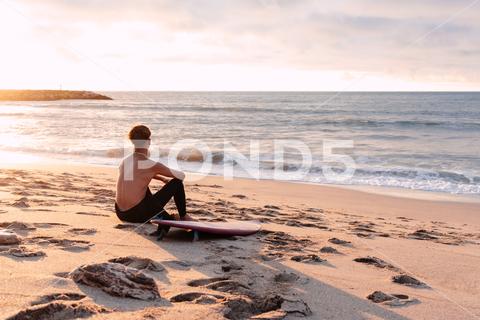 Back view of unrecognizable male surfer with naked torso and surfboard sitting on sandy coast and enjoying picturesque seascape during sunset man, surfer, beach, sunset, surfboard, vacation, relax, summer, seascape, sea, male, enjoy, picturesque, sand, shirtless, coast, ocean, shore, evening, seashore, sundown, nature, tranquil, naked torso, admire, peaceful, water, paradise, wave, coastline, seaside, serene, tropical, twilight, sit, tourism, summertime, exotic, holiday, anonymous, unrecognizable, back view, rest, travel, trip, tourist, hobby, equipment, journey