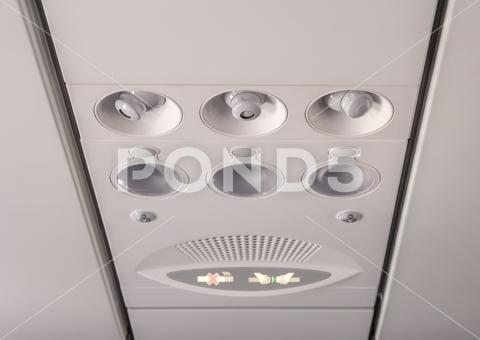 Adjustable lights and air conditioners overhead seat controls of a commercial aircraft in an airplane with no-smoking and seat belt on signs nobody, part, transport, inside, air, travel, transportation, panel, fly, flight, console, airplane, conditioner, sign, cabin, aircraft, plane, light, overhead, control, aviation, conditioning, board, button, lamp, cool, seat, jet, ventilation, closeup, vent, smoke, ceiling, seating, safety, warning, no, plastic, aeroplane, airline, knob, detail, round, symbol, commuter, security, passenger, airliner, background
