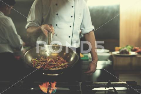 Young male chef flipping vegetables in wok at commercial kitchen Young, male, chef, tossing, vegetables, wok, commercial, kitchen, cooking, pan, food, cook, meal, vegetable, restaurant, gourmet, frying, preparation, professional, culinary, occupation, flipping, healthy, dinner, industry, cuisine, man, job, person, preparing, uniform, toss, stir, stove, young, hotel, profession, working, fried, service, work, fresh, hand, dish, smoke, dieting, burning, catering, nutrition, portrait