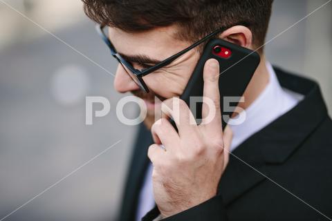 Close up of smiling businessman talking on smartphone. Happy male business professional making a phone call. business, businessman, caucasian, closeup, corporate, eyeglasses, face, happy, headshot, lifestyles, male, man, mobile, office, one, outdoors, people, person, phone, positive, professional, side, smartphone, smiling, standing, talking, technology, using, view, young