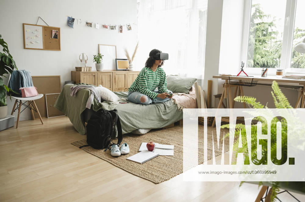 IMAGO Creative, Lifestyle, Gaming Teenage girl wearing virtual reality simulators playing video game with controller at home model released, Symbolfoto property released, ALKF00664
