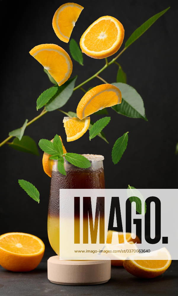 Iced coffee with orange juice in a transparent glass, refreshing bumble coffee on the table Iced coffee with orange juice in a transparent glass, refreshing bumble coffee on the table. Levitating orange slices and mint leaves
