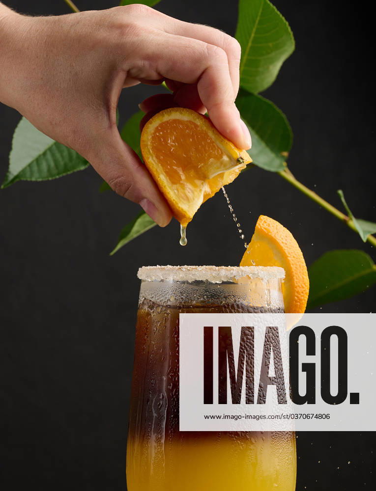 Iced coffee with orange juice in a transparent glass, a woman s hand squeezes an orange slice into a bubble drink Iced coffee with orange juice in a transparent glass, a woman s hand squeezes an orange slice into a bubble drink