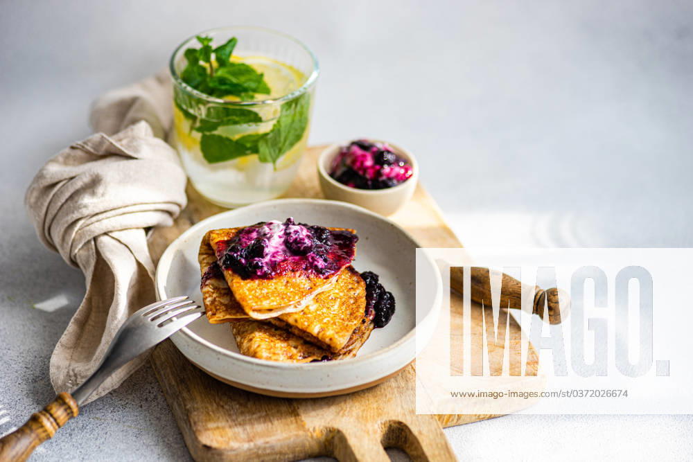 A stack of fresh, homemade crepes topped with blueberry jam and a dollop of sour cream, served with a refreshing mint-infused drink. Model Released AnnaBogush_ID17797_537128_005