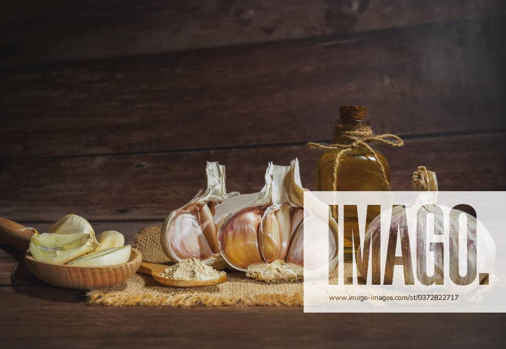 Whole, pulverized and chopped Garlic at a Jute cloth and a Glass bottle with Olive oil at a Wooden table