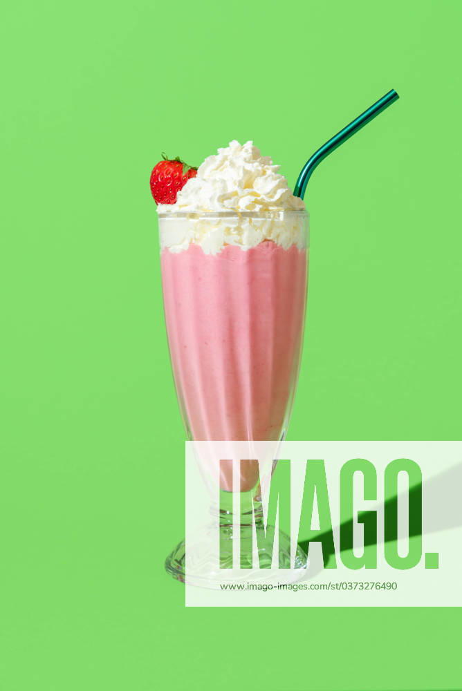 Strawberry milkshake with whipped cream, minimalist on a green background Strawberry flavored milkshake in bright light, minimalist on a green colored table. Delicious homemade milkshake with vanilla ice cream, strawberries and topped with whipped cream.
