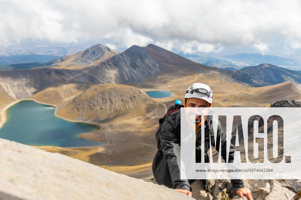A smiling hiker wearing a helmet climbs Nevado de Toluca s rocky terrain with crater lakes in the background under a cloudy sky. Model Released EduardoGavira_ID17888_539292_004