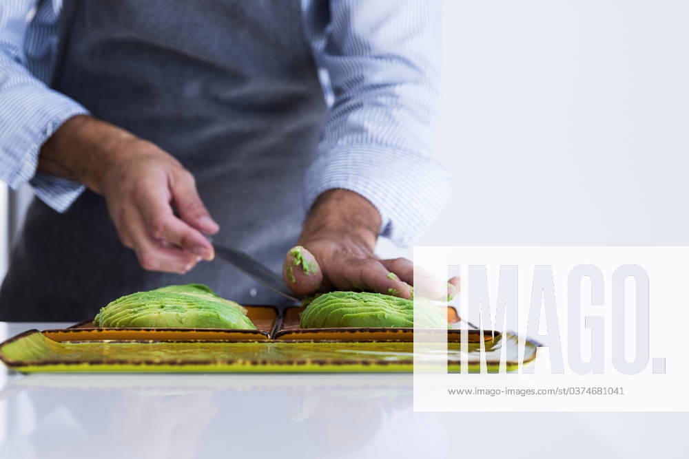 Closeup of crop anonymous private chef in apron cutting avocado with knife while preparing healthy vegetarian breakfast in light kitchen Model Released MartinZubiriaPhotography_ID17004_518468_013