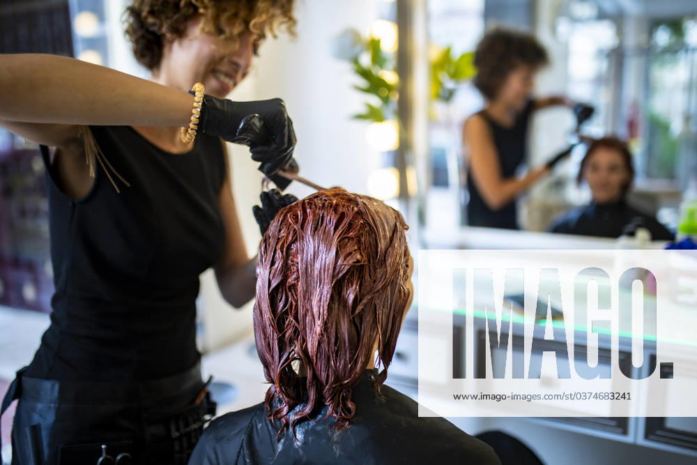 Hair stylist applies dye to client s hair in a salon with a mirror reflection showing work in progress. Model Released PabloGallardo_ID17980_541733_014