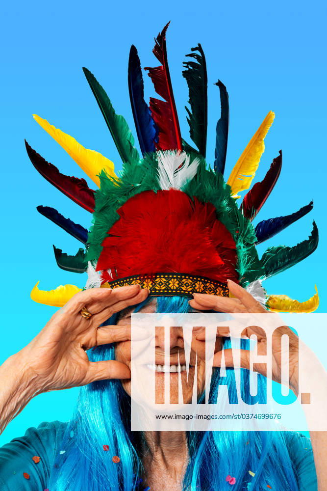 IMAGO Creative, Gesellschaft, Fasching Portrait of smiling senior lady blue in wig with confetti wearing Indian headdress with colorful feathers while standing and touching face against blue background and looking at camera Model Released SergioVictorVega_ID17016_518845_023