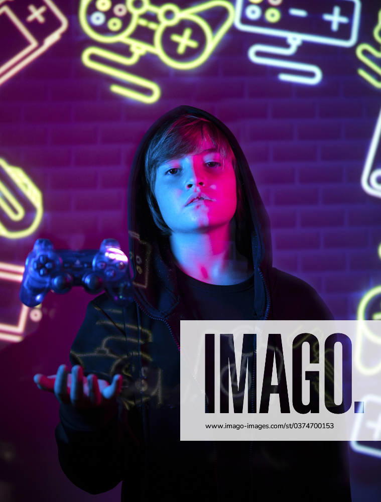 IMAGO Creative, Lifestyle, Gaming A young teen stands holding a game controller, bathed in the vibrant glow of neon lights with gaming symbols in the background. Model Released SergioVictorVega_ID17439_529355_007