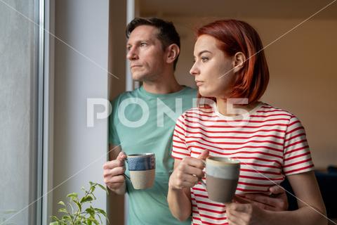 Upset girl and man hold cup of coffee, look out window, sad and anxious. Family problems. Unhappy husband and wife hustle about life and problem solving. Feelings loneliness in couple couple thoughtful thinking looking window coffee cup pensive upset problem home negative relationship lifestyle together wife coffee husband romantic cup tea togetherness drink marriage reflection family boyfriend lonely confusion anxious unhappy worried love trouble indoors guilt despair frustration loneliness sad man girl woman stress solitude sorrow suffering standing emotion