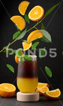 Iced coffee with orange juice in a transparent glass, refreshing bumble coffee on the table. Levitating orange slices and mint leaves glass coffee cold orange slice sweet syrup cool drink espresso ice juice juicy layer morning nobody table yellow levitation mint green beverage black brown bumble caffeine citrus cocktail fresh fruit