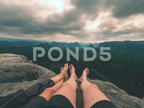 Tired hikers legs without shoes in mountains. Barefoot legs of heterosexual couple. Long forest valley in hilly landscae of nature park. forest edge cliff traveler travel tourist hiker tourist toe tired skin sitting sandstone rock freedom feet comfortable barefoot legs barefoot bare feet knee bandage crossed legs weather watching walker valley shoeless sandstone peak sandstone rock rest outdoor naked feet nail mountain morning moment legs hiking hairy caucasian by foot body backpacker artery agnail couple pair woman man male legs female legs