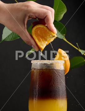 Iced coffee with orange juice in a transparent glass, a woman's hand squeezes an orange slice into a bubble drink orange slice citrus cocktail coffee cold squeeze sweet syrup table yellow beverage black brown bumble caffeine cool drink drop espresso fresh fruit glass hand ice juice juicy layer morning nobody