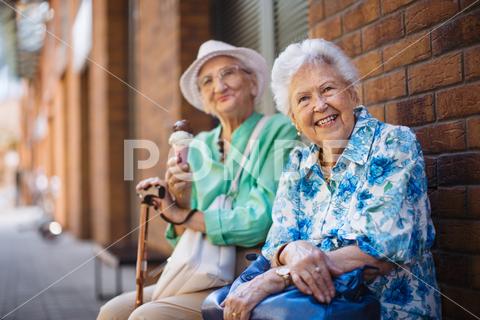 Portrait of two senior female friends in the city, eating ice cream on a hot summer day. Elderly ladies on summer vacation in the city. Pensioners on group trip. Concept of senior vacation and travel groups, clubs. senior city ice cream woman retirement pensioner lifestyle active outdoor elderly old joy vitality happiness smiling eating street togetherness trendy happy holding tourist cone community bonding enjoyment lady older brick wall sitting travel group travel club senior travel traveling vacation chronic illness diabetes heart disease alzheimers disease mental health osteoporosis arthritis dementia hypertension cholesterol depresion rheumatoid arthritis incontinence