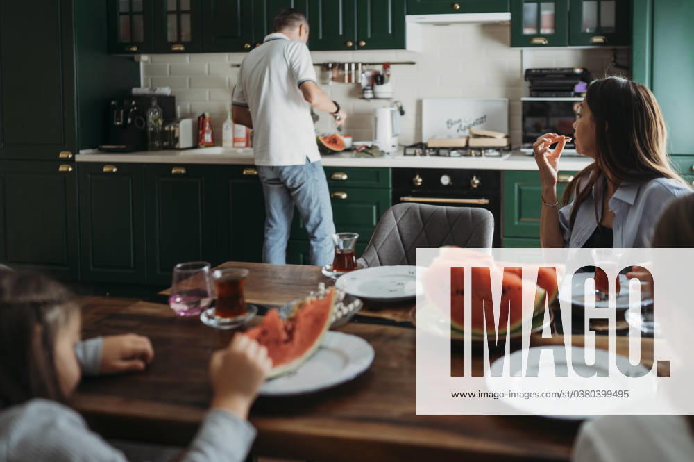 Mother and daughters having lunch at table with man cutting watermelon in kitchen model released, Symbolfoto property released, ANAF02423