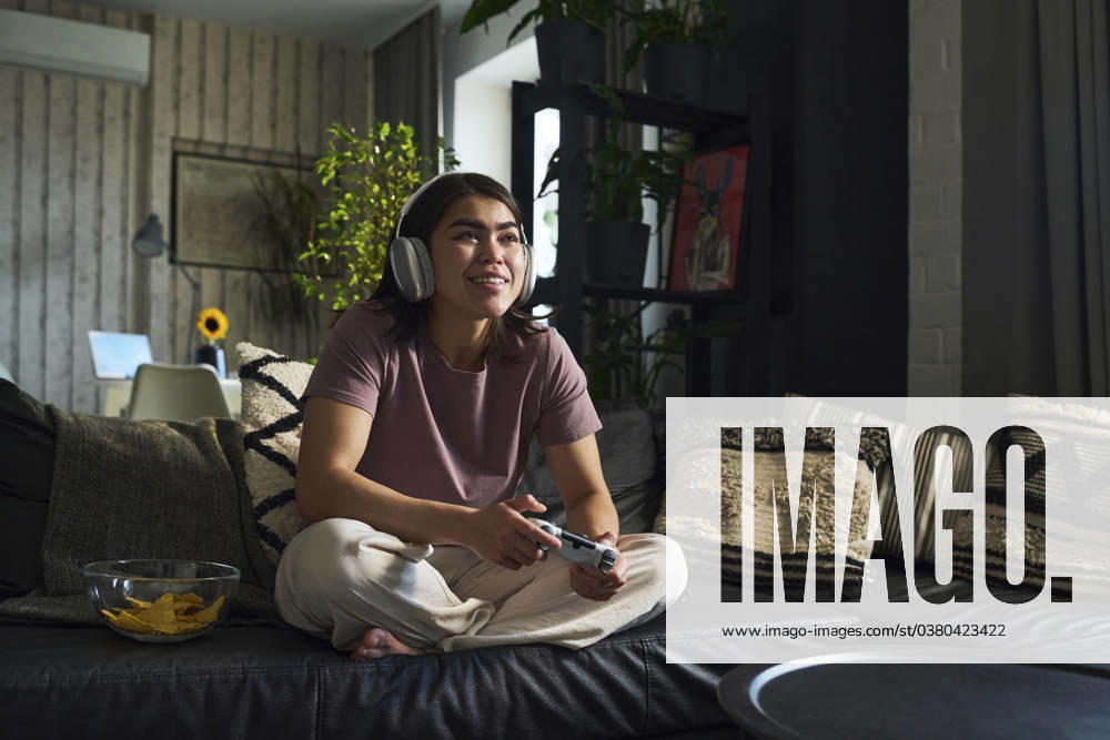 IMAGO Creative, Lifestyle, Gaming Happy young woman playing video game with controller on sofa at home model released, Symbolfoto property released, DSHF01146