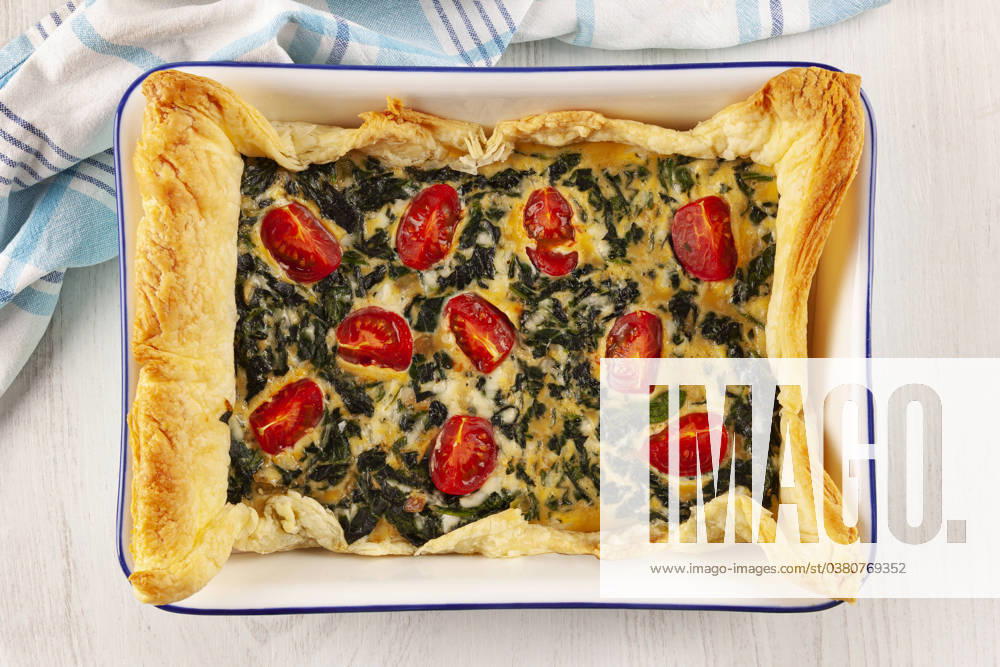 Home made spinach quiche top view. Vegetarian spinach pie or quiche with cheese and tomatoes in a baking dish from above.