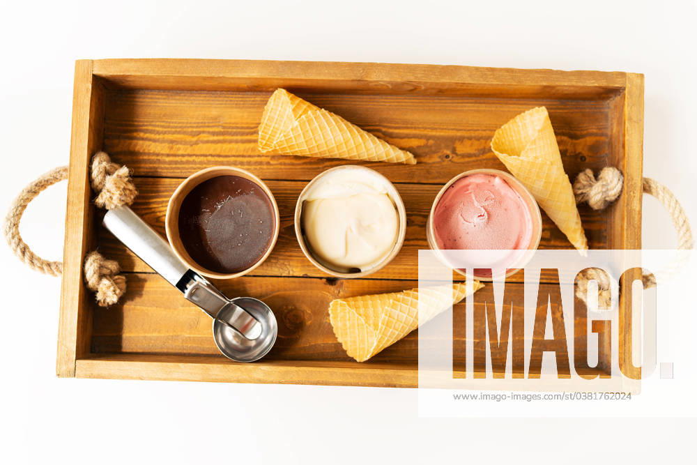 Buckets with different flavors of ice cream, a metal spoon and waffle cups stand on a wooden tray. The concept of healthy and tasty summer food. View from above. Buckets with different flavors of ice cream, a metal spoon and waffle cups stand on a wooden tray. The concept of healthy and tasty summer food. View from above