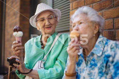 Portrait of two senior female friends in the city, eating ice cream on a hot summer day. Elderly ladies on summer vacation in the city. Pensioners on group trip. Concept of senior vacation and travel groups, clubs. senior city ice cream woman retirement pensioner lifestyle active outdoor elderly old joy vitality happiness smiling eating street togetherness trendy happy holding tourist cone community bonding enjoyment lady older brick wall sitting travel group travel club senior travel traveling vacation chronic illness diabetes heart disease alzheimers disease mental health osteoporosis arthritis dementia hypertension cholesterol depresion rheumatoid arthritis incontinence