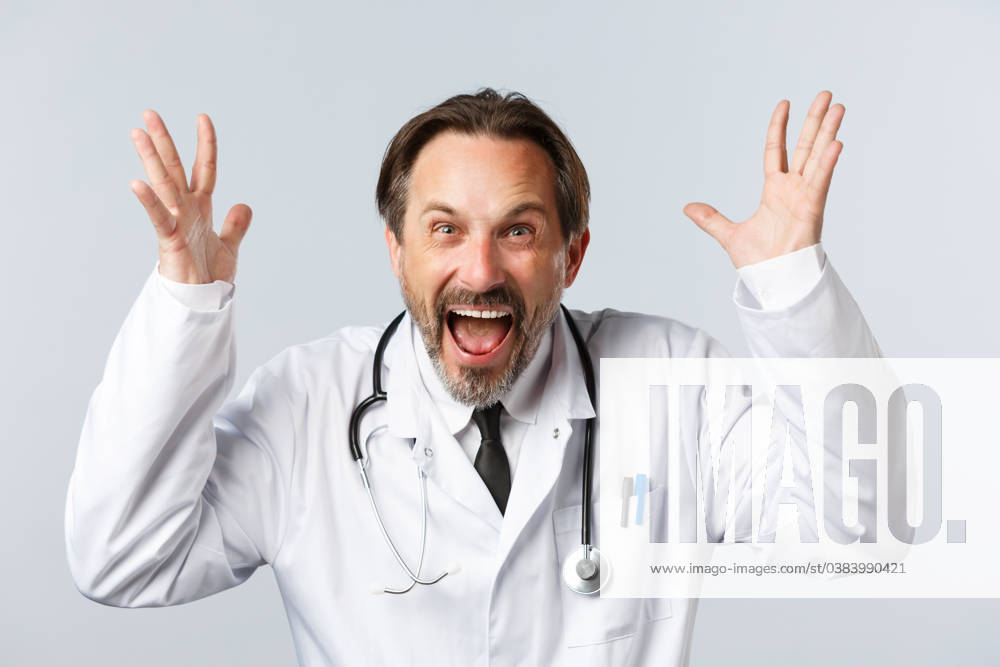 Covid-19, preventing virus, healthcare workers and vaccination concept. Close-up of mad outraged doctor in white coat, raising hands up and shouting furious, being angry Covid-19, preventing virus, healthcare workers and vaccination concept. Close-up of mad outraged doctor in white coat, raising hands up and shouting furious, being angry. ,model released, Symbolfoto