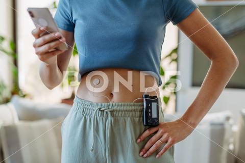 Close up of diabetic woman with insulin pump. Young woman with type 1 diabetes at home. young woman diabetic healthcare diabetes smart phone insulin pump continuous glucose monitor chronic illness social media sharing health technology medical device confident type 1 diabetes type 2 diabetes living with diabetes empowerment lifestyle beauty acceptance chronic disease awareness positivity treatment glucose blood sugar insulin therapy digital health self-love chronic condition patient advocate online community real-life strength body positivity National Diabetes Month november World Diabetes Day