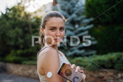 Portrait of woman with diabetes connecting her smartphone to continuous glucose monitor sensor before exercising. Diabetic woman checking her blood sugar levels in real time before running. diabetic woman preparing exercise outdoor city young running continuous glucose monitor health sensor diabetes management lifestyle urban active medical device training health-conscious endurance technology glucose diabetes sport connecting motivation chronic condition routine mobile app street workout modern health determination resilience challenge medicine therapy adaptation empowerment increase insulin decrease insulin adjust physical activity affecting ketones screen display copy space National Diabetes Month november World Diabetes Day