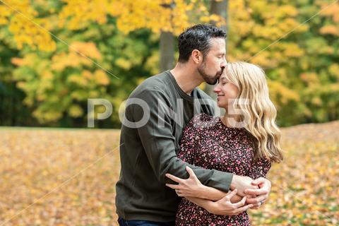 Husband embracing wife, kissing her forehead, eyes closed hugging husband kissing wife love happiness togetherness outdoors leaves embrace loving relationship woman man couple fall seasons autumn mother father parenthood family time laughter together mom dad white caucasian playful joy giggles laughing hugs kiss outside park marriage smiling smile eyes closed southington connecticut united states thirties generation x 36-39 years old two people male female