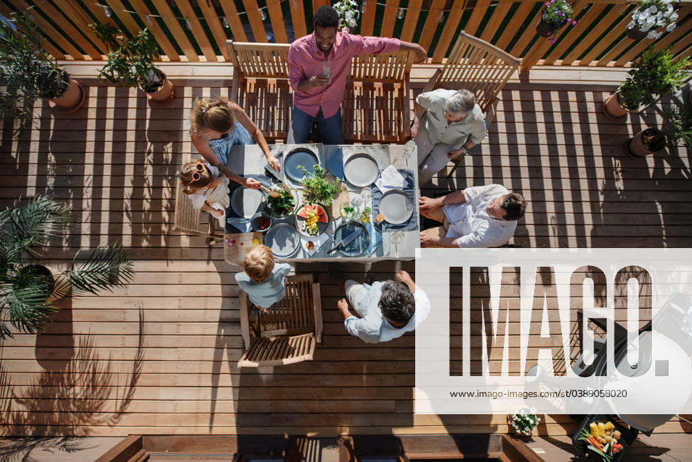 Top view of 3 generations family eating at barbecue party dinner on patio, people sitting at table on patio with grill. A top view of 3 generations family eating at barbecue party dinner on patio, people sitting on patio with grill. model released