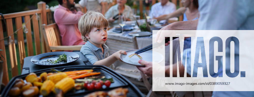 Father putting grilled meat and vegetable on plate to his son during family summer garden party. A father putting grilled meat and vegetable on plate to his son during family summer garden party. model released