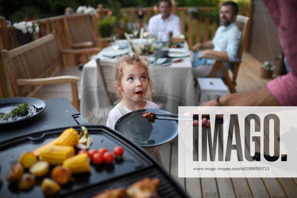 Father putting grilled meat and vegetable on plate to his daughter during family summer garden party. A father putting grilled meat and vegetable on plate to his daughter during family summer garden party. model released