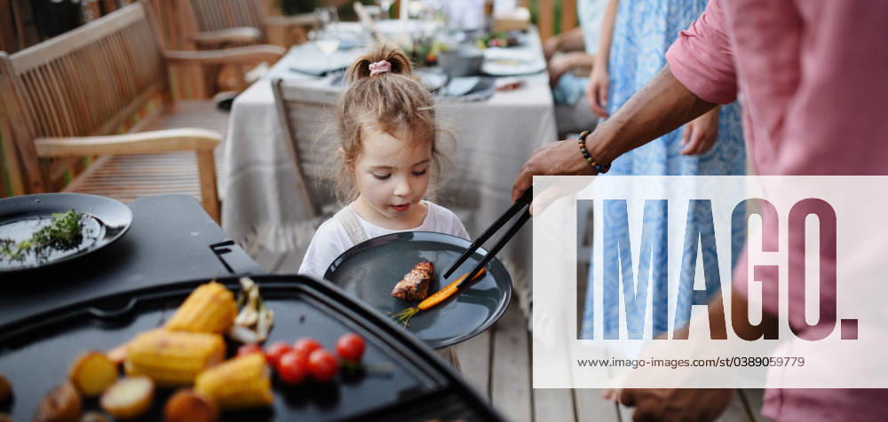 Father putting grilled meat and vegetable on plate to his daughter during family summer garden party. A father putting grilled meat and vegetable on plate to his daughter during family summer garden party. model released