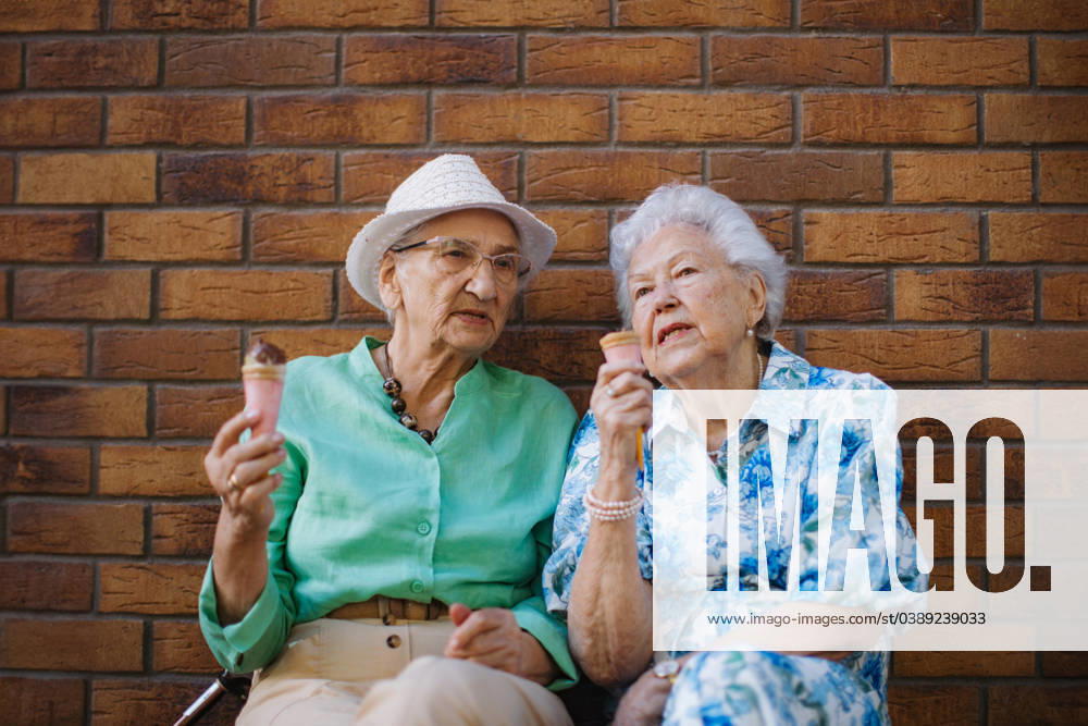 Portrait of two senior female friends in the city, eating ice cream on a hot summer day. Portrait of two senior female friends in the city, eating ice cream on a hot summer day. Elderly ladies on summer vacation in the city. Pensioners on group trip. Concept of senior vacation and travel groups, clubs. model released