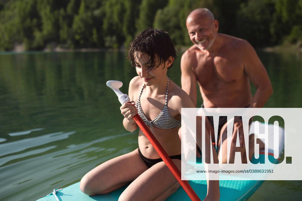 Happy preteen girl with grandfather on summer holiday by lake, paddleboarding. A happy preteen girl with grandfather on summer holiday by lake, paddleboarding. model released