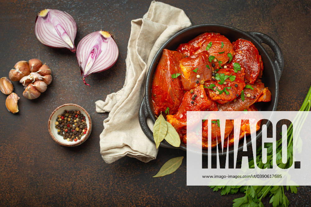 IMAGO Creative, Herbst, Food, Gulasch Raw uncooked chopped pieces of meat marinated with seasonings and parsley in black casserole dish top view on dark rustic background. Cooking ragout stew with marinated meat fillet pieces Raw uncooked chopped pieces of meat marinated with seasonings and parsley in black casserole dish top view on dark rustic background. Cooking ragout stew with marinated meat fillet pieces.