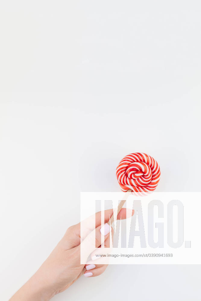 Woman hand with red lollipop Woman hand with pastel manicure polish holding bright red swirling lollipop isolated on white background copy space minimalism style. Template for feminine social media. Fun and celebration concept