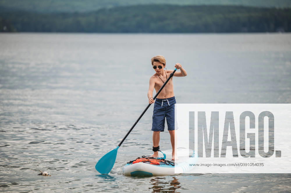 IMAGO Creative, Jahreszeit Sommer, Sommerferien Tween boy in sunglasses paddle boarding Wolfeboro, New Hampshire, United States R_ERBU231220-1310577-01 ,model released, Symbolfoto